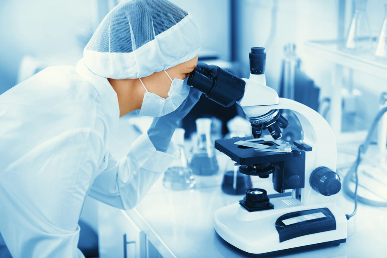 Young woman medical researcher looking through microscop slide in the life science