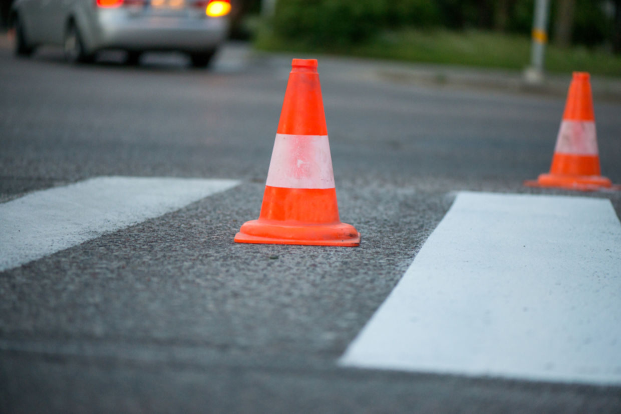 Macro shot of road traffic cones with orange and white stripes standing on street on gray asphalt during road construction works. Just painted white street lines on pedestrian crossing Macro shot of road traffic cones with orange and white stripes standing on street on gray asphalt during road construction works. Just painted white street lines on pedestrian crossing