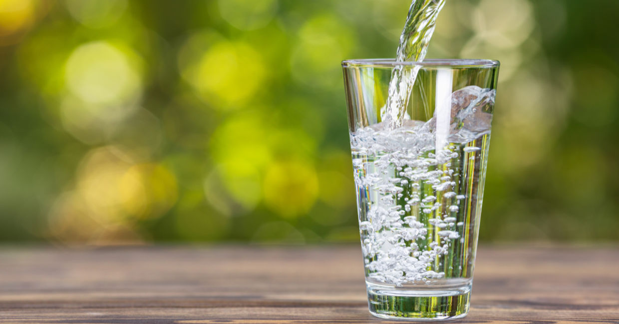 Drinking water from jug pouring into glass on wooden table outdoors