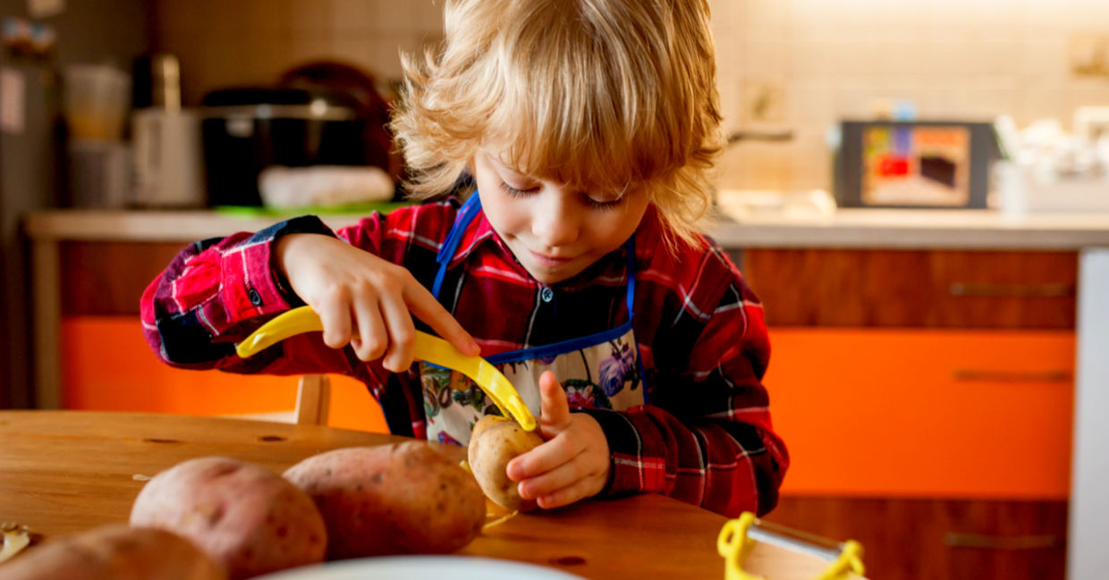 A little kid is carefully peeling potatoes in her kitchen. A little kid is carefully peeling potatoes in her kitchen.