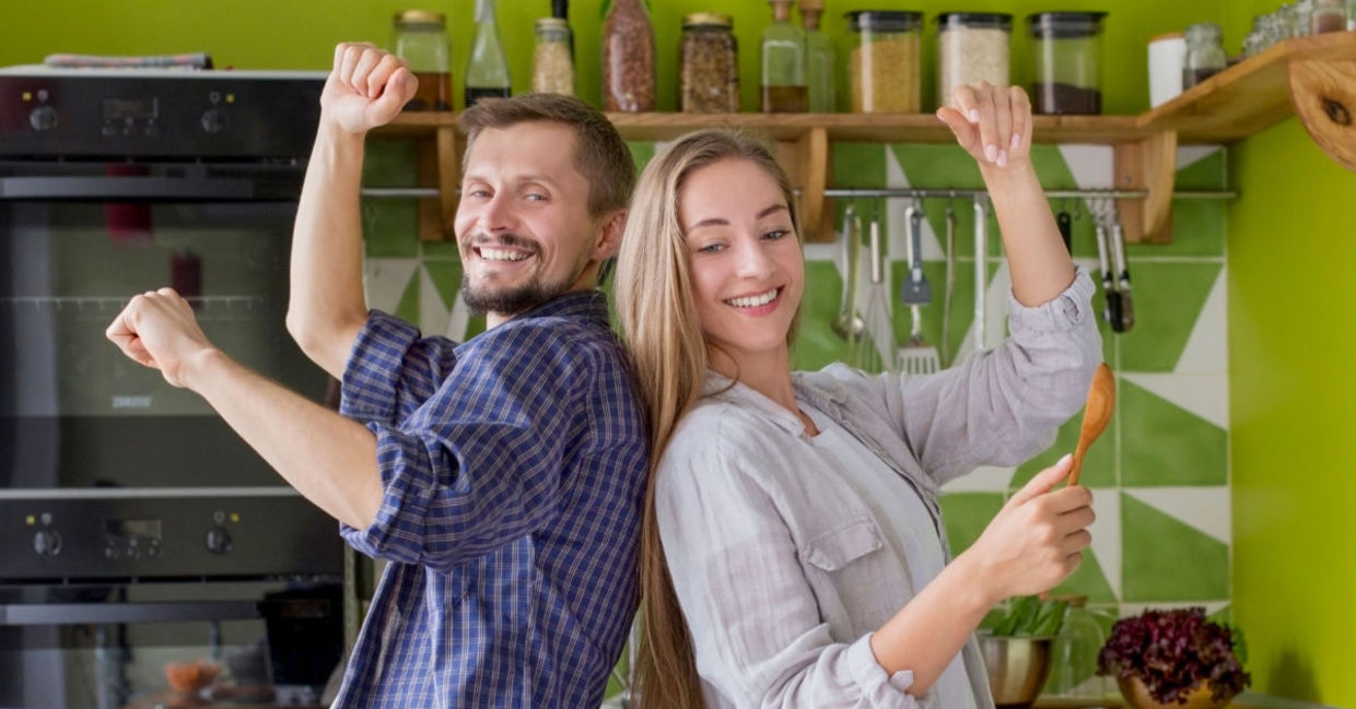 A couple cooks while they dance to music. A couple cooks while they dance to music.