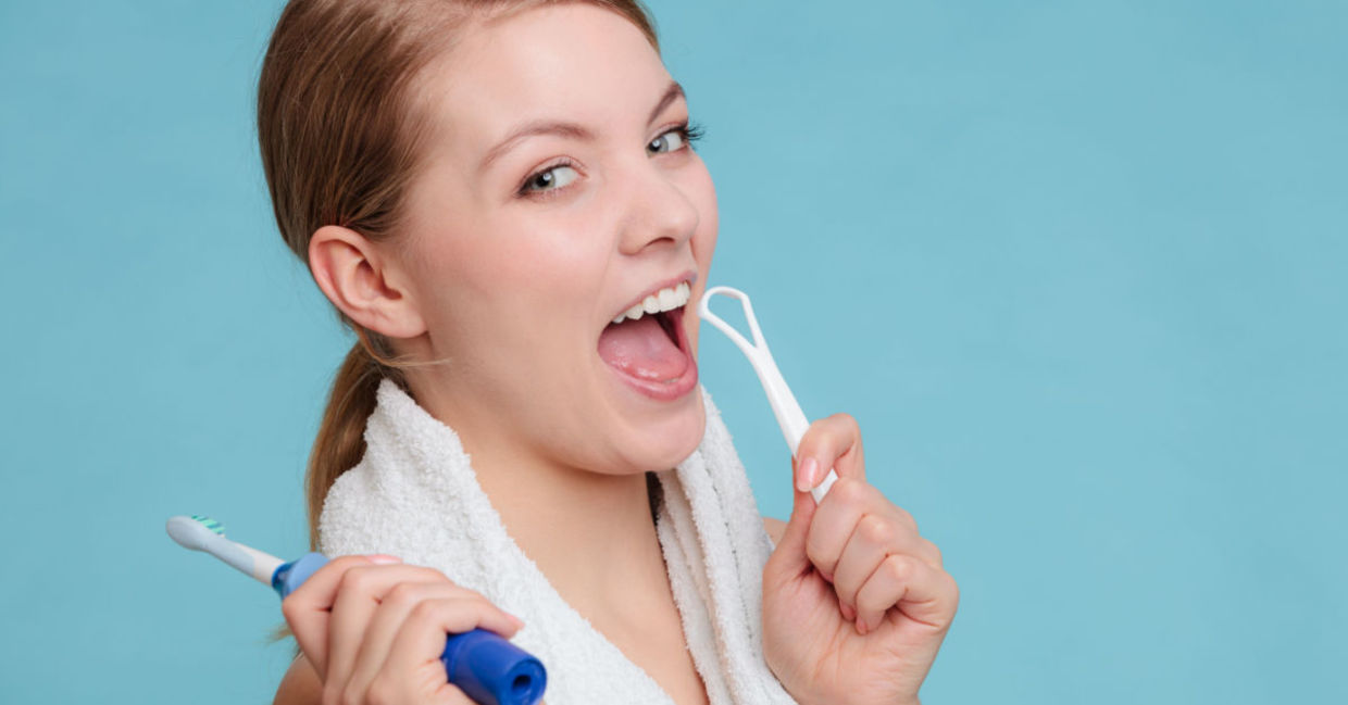 A woman with an electric toothbrush and tongue scraper. A woman with an electric toothbrush and tongue scraper.